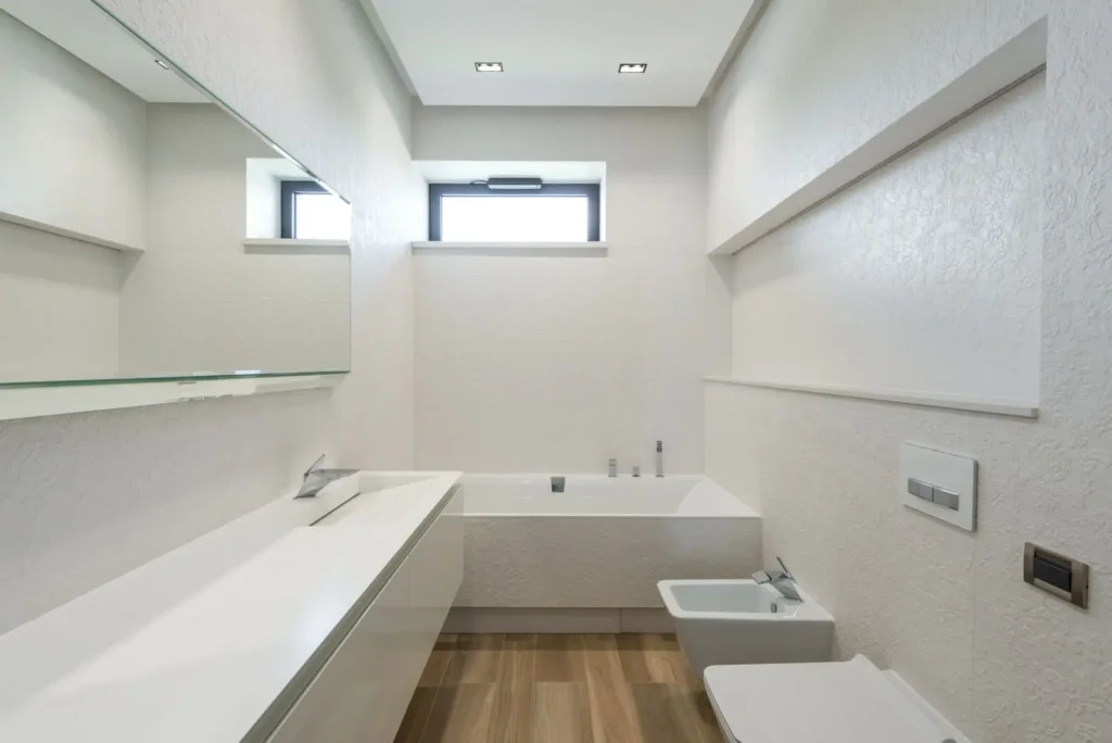 Bright white bathroom with a high window, bathtub and long vanity