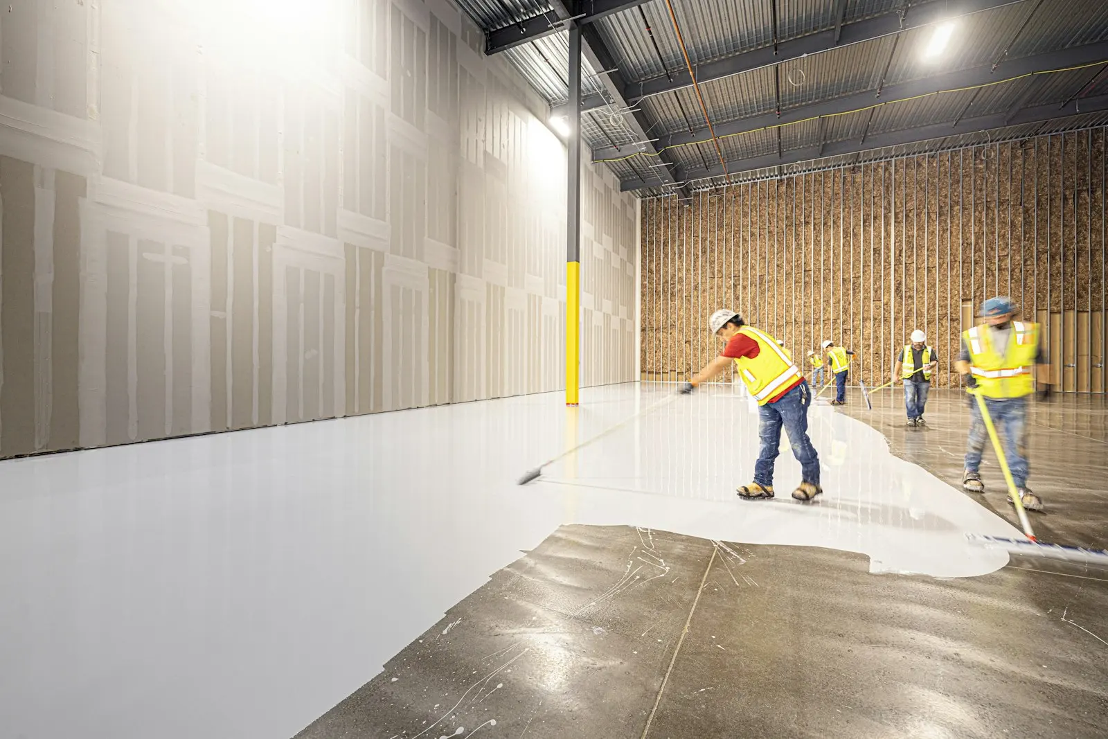 Workers in hi-vis spreading a white epoxy coating across a large concrete floor