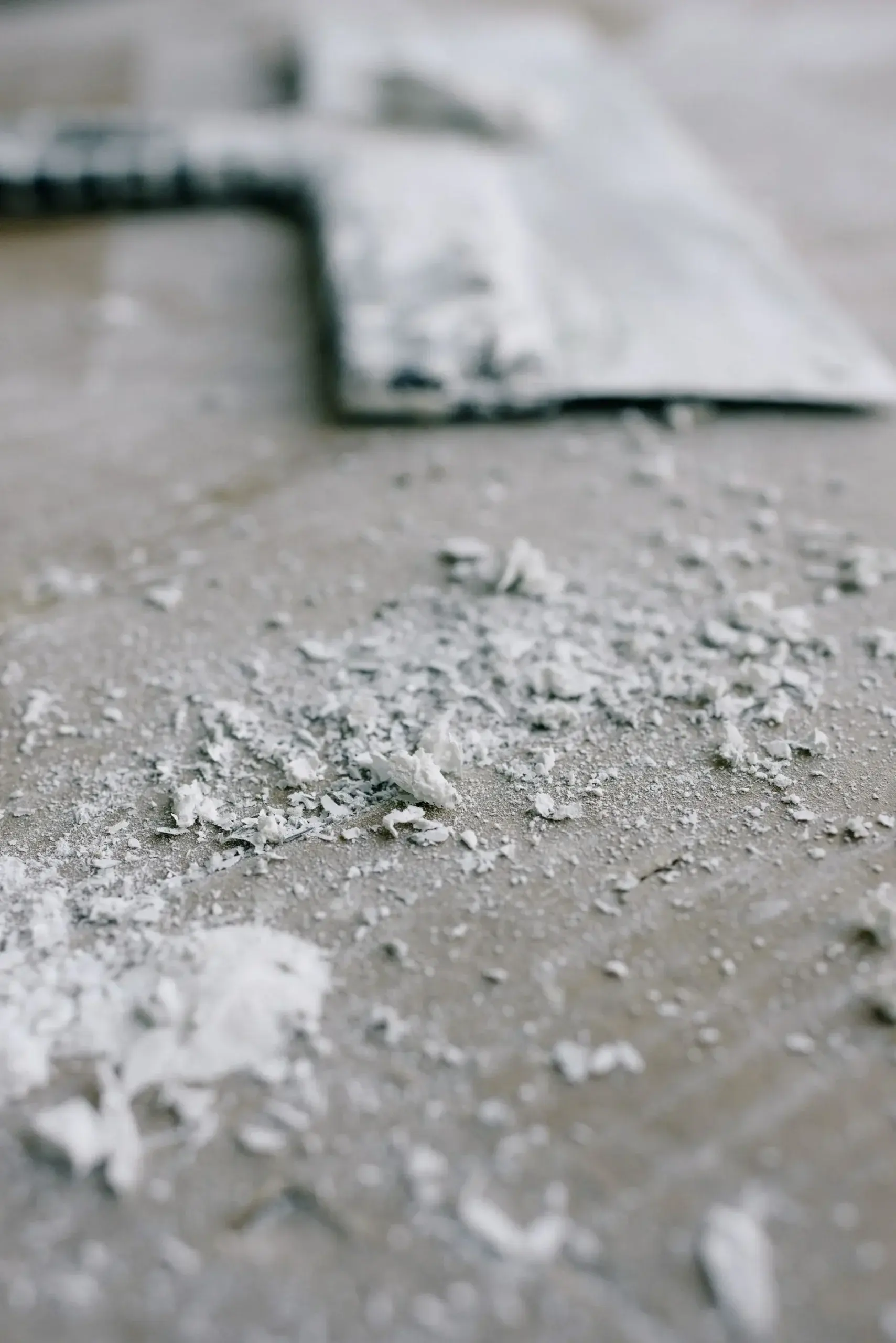 Paint scraper resting on a floor covered in flakes of old white paint