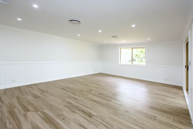 Empty open-plan room with white walls, wainscoting and a timber-look floor