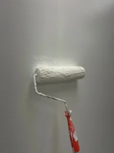 Paint roller applying a fresh coat of white paint to a smooth wall