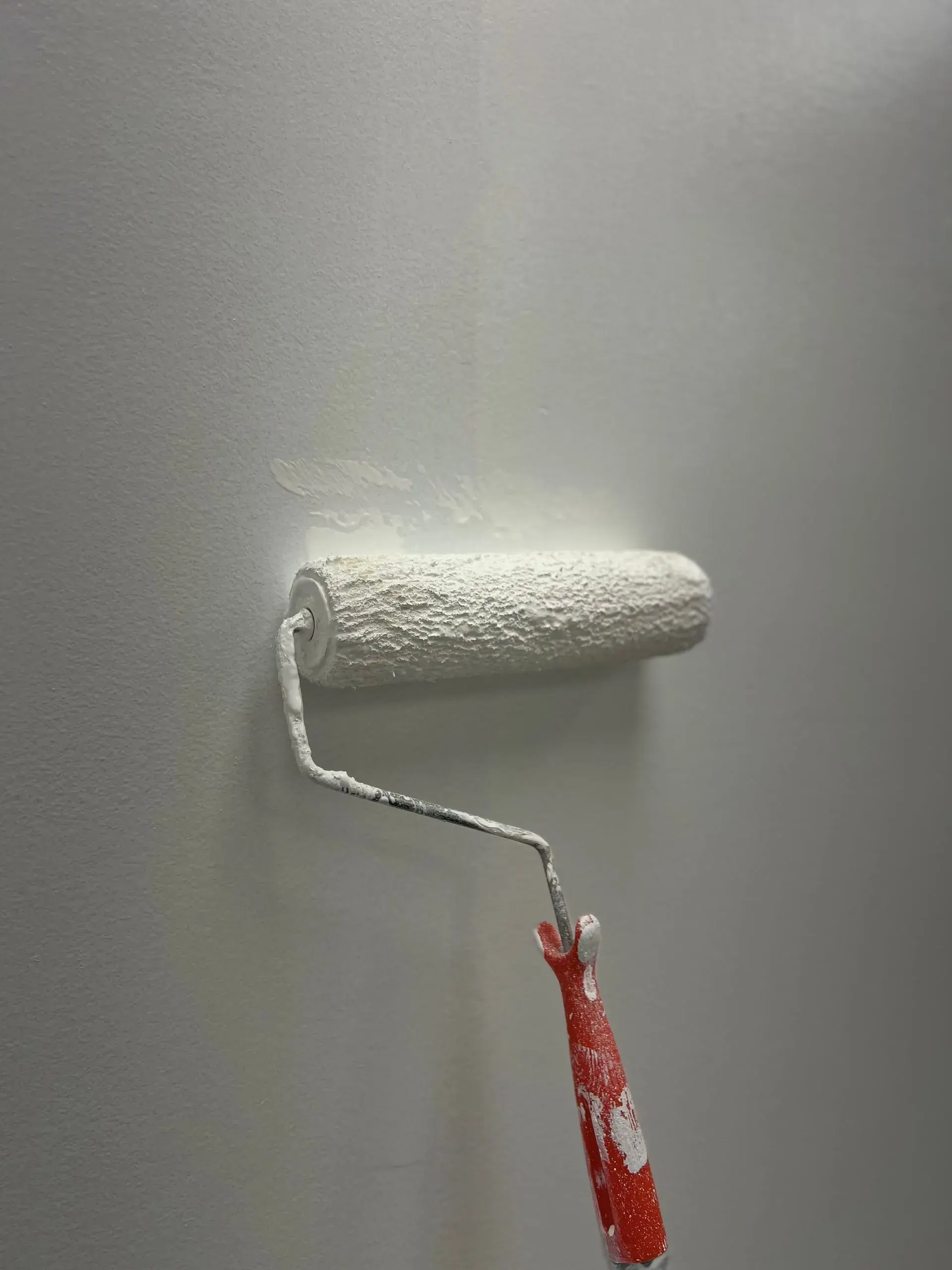 Paint roller applying a fresh coat of white paint to a smooth wall